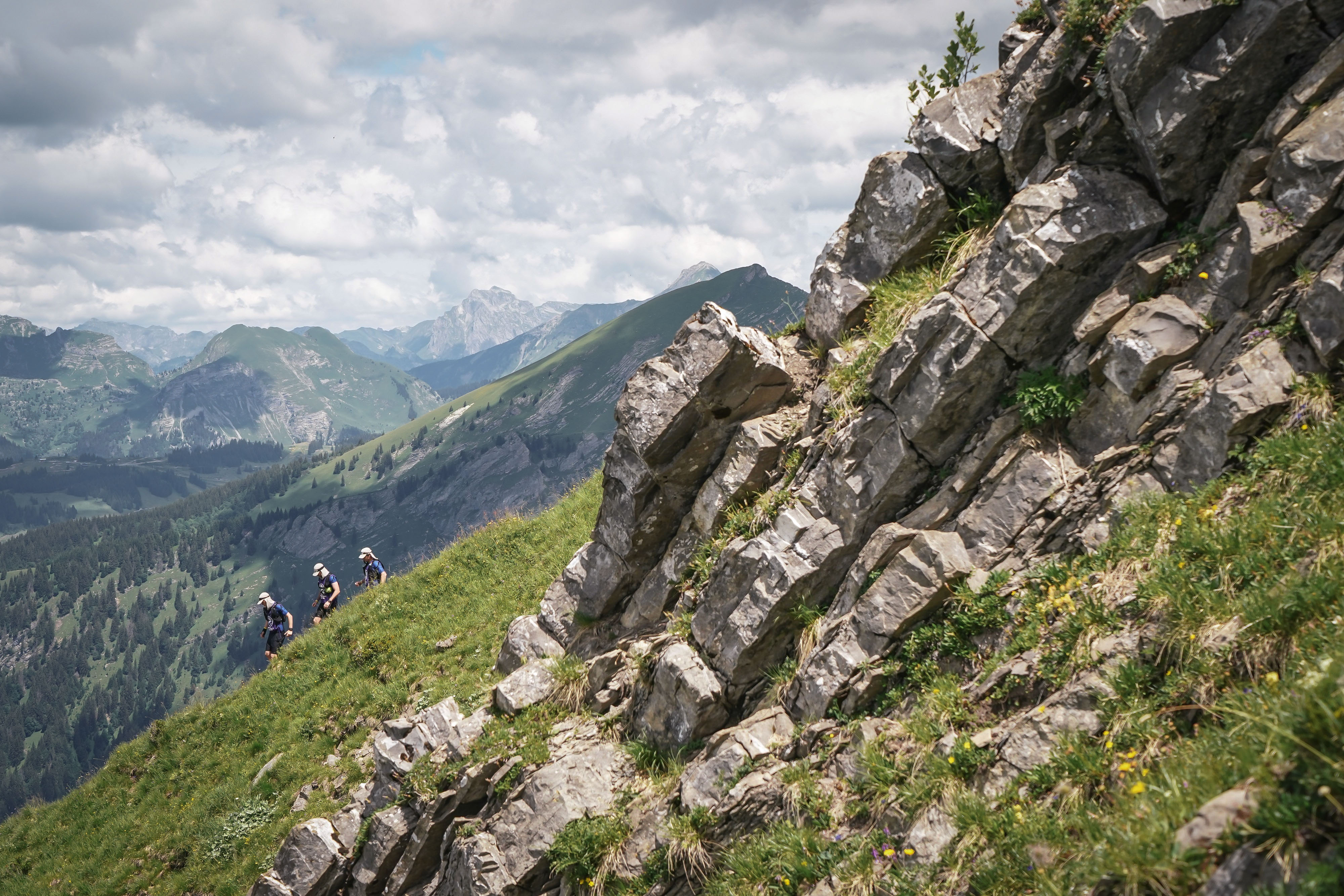 Athletes crossing an alpine ridge near the Grand Combin massif, small against the mountain landscape